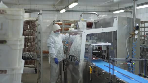 Le travailleur du département des saucisses se tient près du dispositif automatique pour emballer les saucisses dans un emballage sous vide. — Video