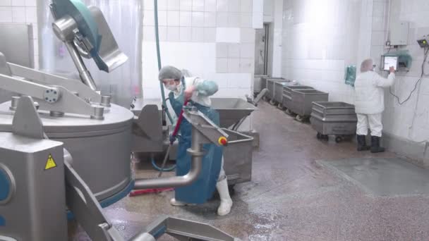 Werknemer wast de apparatuur met water uit een slang op de onderneming. Sanitaire reiniging van worstproductieapparatuur bij de onderneming. — Stockvideo