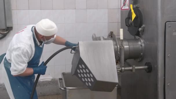 L'employé lave l'équipement à l'eau d'un tuyau d'arrosage de l'entreprise. Nettoyage sanitaire des équipements de production de saucisses dans l'entreprise. — Video