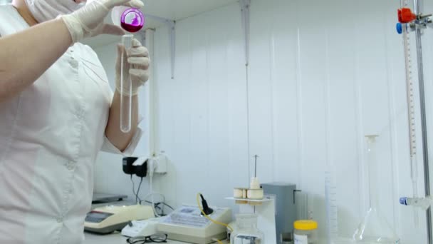 Bir laboratuvar çalışanı cam şişeden pembe bir madde döker ve plastik bir ölçü kabında sallar. Araştırmacı laboratuarda bir deney yapıyor. — Stok video