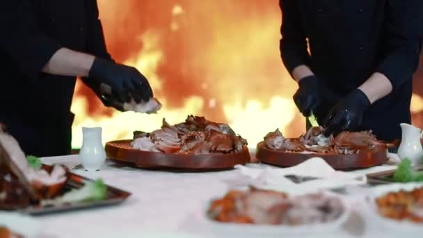 Los chefs cortan carne recién cocinada en el fondo de una gran pantalla con un fuego artificial. Entorno discográfico. Luz de diferentes colores ilumina la escena . — Vídeos de Stock