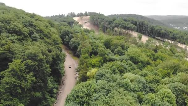 Vista aérea superior Carro está dirigindo em uma estrada ruim na floresta entre as árvores, contornando buracos na estrada . — Vídeo de Stock