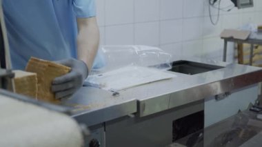 Fırın işçisi plastik torbalara dilimlenmiş ekmek paketliyor. Ekmek üretimi ve ambalajı.