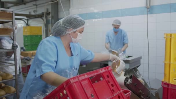 Een werknemer die in een bakkerij werkt. De bakker spreidt het gesneden brood uit op een automatische verpakkingsmachine in de fabriek — Stockvideo