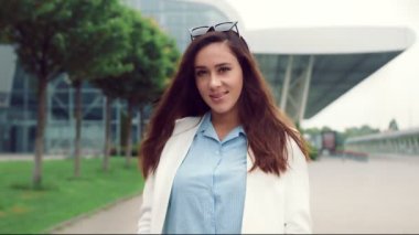 Siyah saçlı, gülümseyen ve kameraya bakan beyaz bir kadının portresi. Sokaktaki kız kameraya gülümseyen modern iç mekanların arka planında..