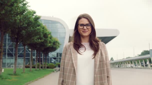 Ritratto di una bella donna caucasica con i capelli neri che sorride e guarda la macchina fotografica. Ragazza per strada su uno sfondo di interni moderni sorridente alla fotocamera. — Video Stock