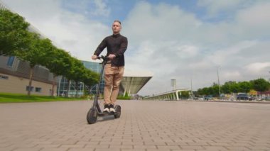Başarılı genç adam iş merkezinin yakınında elektrikli scooter kullanıyor. Elektrikli scooter kullanan gençler.