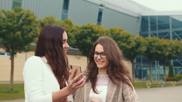 Las amigas felices navegan por el contenido de un teléfono móvil y sonríen sinceramente. Dos gemelos riendo mirando el celular . — Vídeos de Stock