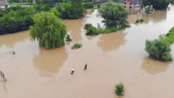 Украина. Галич, 24 июня 2020 года. Два велосипедиста пересекают тропу в воде на дороге после наводнения. Затопленная дорога. Наводнения и стихийные бедствия . — стоковое видео