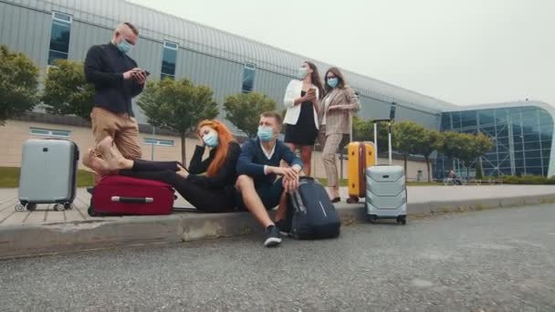 Un gruppo di turisti con maschere mediche vicino al terminal dell'aeroporto sta aspettando il volo. Un gruppo di turisti in attesa con i bagagli. Il problema dei voli durante un'infezione virale — Video Stock