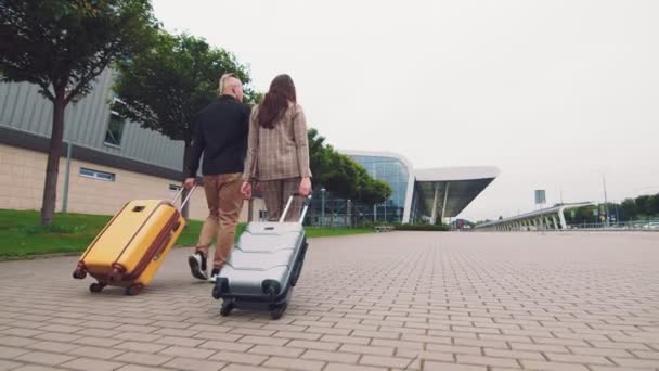 Dois jovens apaixonados viajando. Casal feliz vai para o terminal do aeroporto com bagagem. Jovens embarcam em uma viagem de mãos dadas rumo ao terminal do aeroporto . — Vídeo de Stock