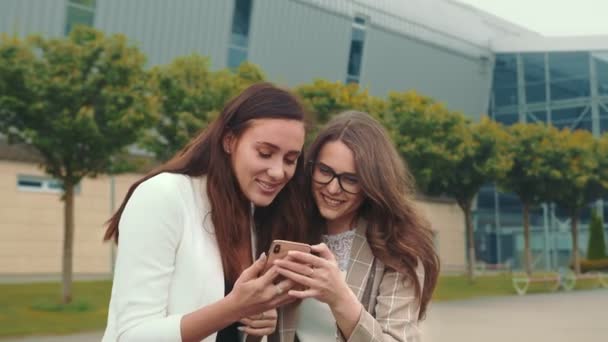 Gelukkige vrouwelijke vrienden bladeren door de inhoud van een mobiele telefoon en glimlachen oprecht. Twee tweelingen lachen terwijl ze naar een mobieltje kijken.. — Stockvideo