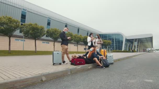 Un groupe de touristes portant des masques médicaux près du terminal de l'aéroport attend le vol. Un groupe de touristes qui attendent avec des bagages. Le problème des vols lors d'une infection virale — Video