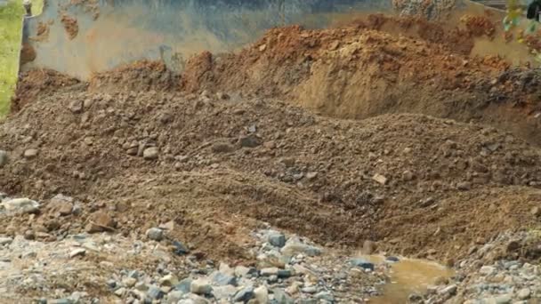 Primer plano del terreno nivelando una excavadora. Piedras y arcilla llenan los huecos vacíos de la carretera de montaña con una excavadora — Vídeo de stock