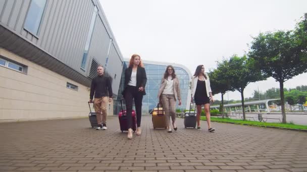 A repülőtér termináljának hátterében poggyásszal sétáló turisták csoportja. Egy csapat fiatal üzletember poggyásszal elrepült egy új városba, és egy új modern repülőtér hátterében sétáltak. — Stock videók