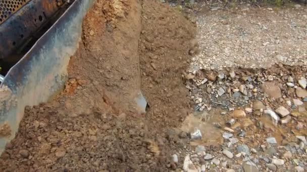 Primer plano del terreno nivelando una excavadora. Piedras y arcilla llenan los huecos vacíos de la carretera de montaña con una excavadora — Vídeos de Stock