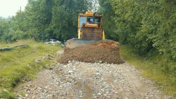 Bir buldozer düzeyi ve dağlardaki bir yolu onarıyor. Buldozer yavaşça ilerliyor ve yoldaki taşları örtüyor.. — Stok video