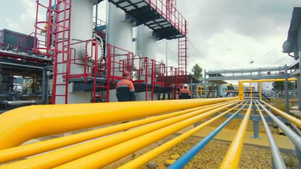 Gasman con una maschera protettiva che cammina lungo la stazione di produzione del gas e la ispeziona. Linee gialle di distribuzione del gas lungo le quali è distribuito il flusso del gas. — Video Stock