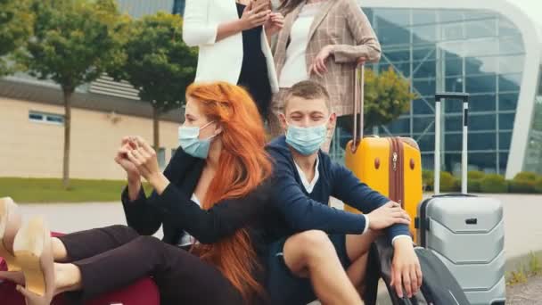 Sebuah kelompok turis bertopeng medis yang bersenang-senang menunggu penerbangan mereka. Gadis muda yang bahagia dengan topeng medis duduk berdansa dengan kebahagiaan. Penerbangan menunggu. — Stok Video