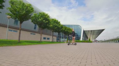 Başarılı genç adam iş merkezinin yakınında elektrikli scooter kullanıyor. Elektrikli scooter kullanan gençler.