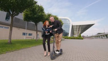İşadamı elektrikli scooter kullanırken belgeleri imzalıyor. Sekreter belgeleri, elektrikli scooter kullanırken evrakları imzalayan bir iş adamının kocasına veriyor..