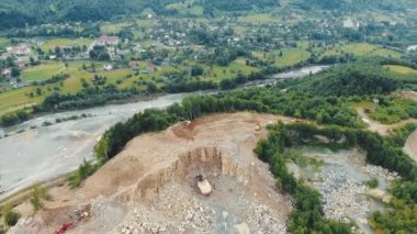 Taşların ve diğer kayaların mayınlandığı dağlardaki bir taş ocağının üzerinden hava manzaralı uçuş. Bir dağ nehrinin arka planındaki taş ocağında çalışan ağır makineler..