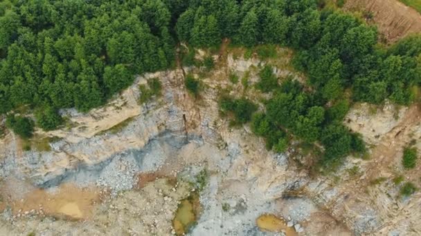 Luftaufnahme des obersten Steinbruchs in den Bergen zum Abbau von Steinen. Felsiges Gelände mit einer Klippe am Rande des Berges, wo grüne Bäume wachsen. — Stockvideo