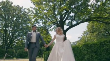 Genç, aşık bir çift. Yeni evliler. Yeşil ağaçların arka planında güneşli bir parkta yürüyorlar. Gelinler güneşli bir günde parkta yürürler..
