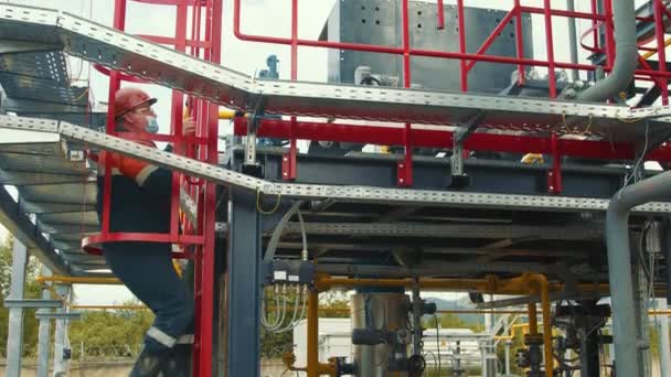 Gasman met een beschermend masker loopt langs het benzinestation en inspecteert het. De gasproductiewerker inspecteert de metalen structuren van het gasdistributiecomplex. — Stockvideo