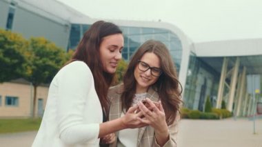 Mutlu bayan arkadaşlar cep telefonunun içeriğini inceler ve içtenlikle gülümserler. İki ikiz cep telefonuna bakıp gülüyor..