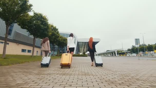 Tres niñas felices se van de viaje. Las mujeres caminan con el equipaje en la mano hasta el aeropuerto . — Vídeos de Stock