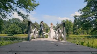 Yeni evliler düğün günlerinde gölün kıyısındaki tahta bir köprüde duruyorlar.