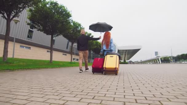 Eine Frau trägt zwei Koffer zum Flughafenterminal, ein Mann einen Regenschirm. Die Priorität eines Mannes in der Familie. Beziehungsprobleme eines jungen Paares. — Stockvideo