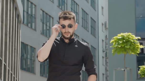 Портрет молодого успішного бізнесмена, який знімає окуляри і дивиться на камеру. харизматичний недбалий чоловік в чорному одязі з сексуальними окулярами . — стокове відео