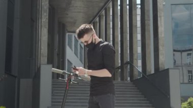 Elektrikli scooter kiralama. Koruyucu maskeli bir adam elektrikli scooter 'a yaklaşır ve tasmasını takar. Ekolojik şehir ulaşımı. Tıbbi maskeli bir adam elektrikli scooterın kilidini açıyor.