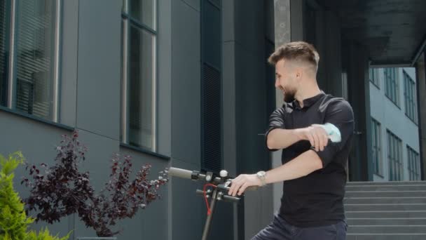 Conclusão da quarentena. Um homem está perto de uma scooter elétrica ambientalmente amigável e felizmente remove uma máscara protetora médica de seu rosto e sorri . — Vídeo de Stock