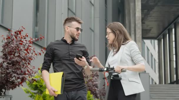 Dos jóvenes modernos de éxito, un hombre de negocios y una mujer de negocios, se comunican entre sí, sonríen, miran el teléfono inteligente, se comunican con gadgets . — Vídeo de stock