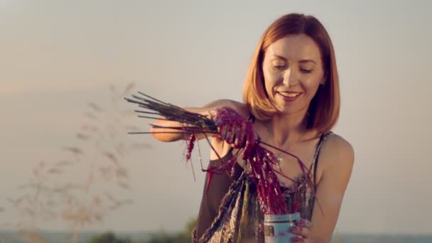 Ansiktet på en kvinna som ler medan hon målar en bild med en improviserad handfull vete indränkt i färg. Pervumens ritar en bild på ett fält vid solnedgången med vetefärg. — Stockvideo