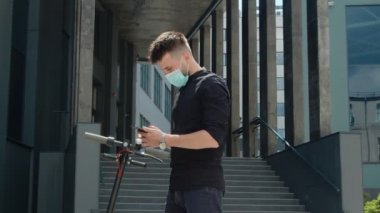 Elektrikli scooter kiralama. Koruyucu maskeli bir adam elektrikli scooter 'a yaklaşır ve tasmasını takar. Ekolojik şehir ulaşımı. Tıbbi maskeli bir adam elektrikli scooterın kilidini açıyor.