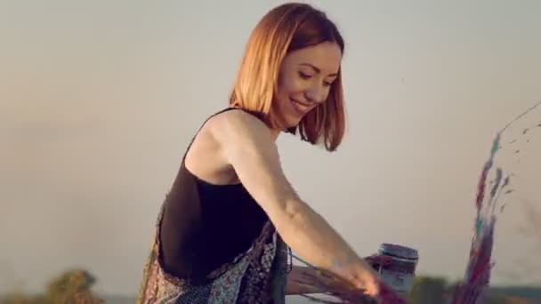 Tvář ženy, která se usmívá, zatímco maluje obraz s improvizovanou hrstí pšenice nasáklé barvou. Pervumens kreslí obrázek na poli při západu slunce s pšeničnou barvou. — Stock video