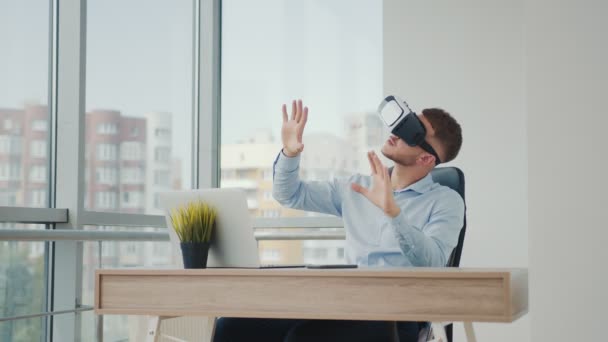 A young man sitting at a desk in the office uses augmented reality glasses to work on business projects in various fields. — Stock Video
