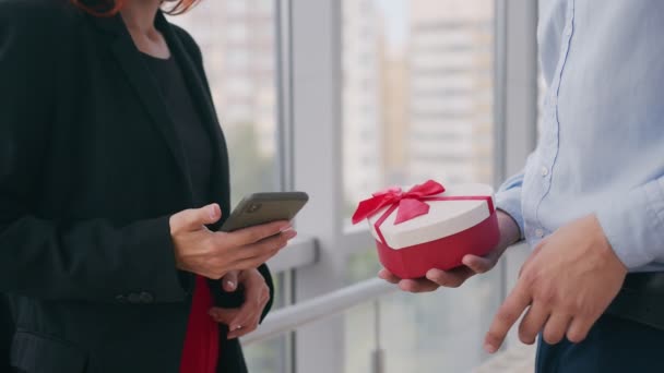 Close-up van een man die een doos opent met een cadeau voor een meisje Een vrouw die aan de telefoon spreekt krijgt een cadeau van haar man en verheugt zich over het geschenk dat ze op kantoor heeft ontvangen. — Stockvideo