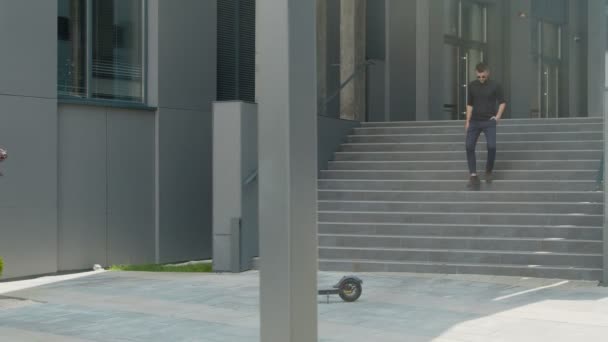 市内の近代的な交通手段として電動スクーターを使用する若い男。男性実業家が電動スクーターに近づき、ビジネスのためにそれに乗る. — ストック動画