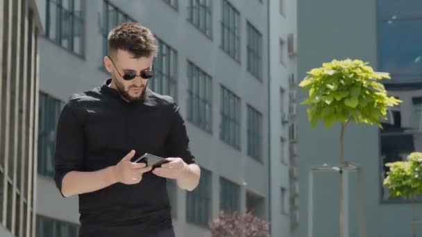 Portrait of a young businessman with glasses holding a mobile gadget receives an important message from which he rejoices and smiles. Happy businessman rejoices in success working with mobile phone in — Stock Video