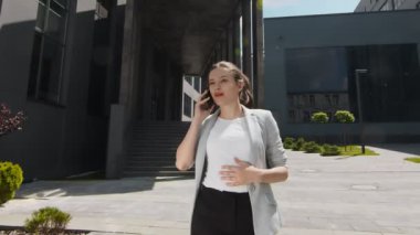 Şehir merkezinde modern evlerin arasında çalışan ve cep telefonuyla konuşan bir iş kadını. Elinde akıllı telefonu olan modern bir kadın gülümser ve çalışır..