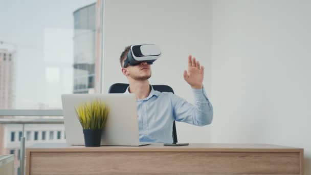 A young man sitting at a desk in the office uses augmented reality glasses to work on business projects in various fields. — Stock Video