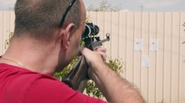 Optik tüfek görüşüne bakarken doğaçlama bir kağıt hedefe nişan alan bir adamın yüzünü kapatın..