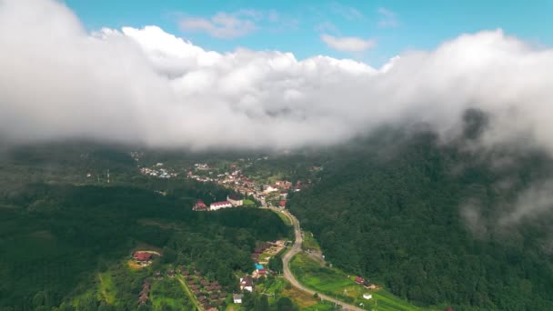 Luftaufnahme Flug über die Wolken, durch die man das Dorf zwischen den Bergen sehen kann. Blick von oben auf die Wolken, die die Berge und Siedlungen in den Bergen bedecken. — Stockvideo
