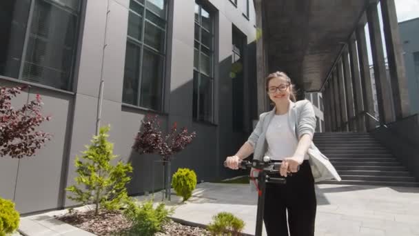 Wanita muda yang sukses mengendarai skuter listrik pada hari yang cerah dan menikmati hidup di latar belakang perkebunan hijau yang indah di taman teknologi. — Stok Video