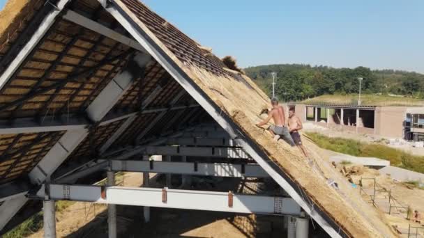 Uitzicht vanuit de lucht op het dak van een groot huis met droog stro en hooi. Werknemers die het dak installeren. — Stockvideo